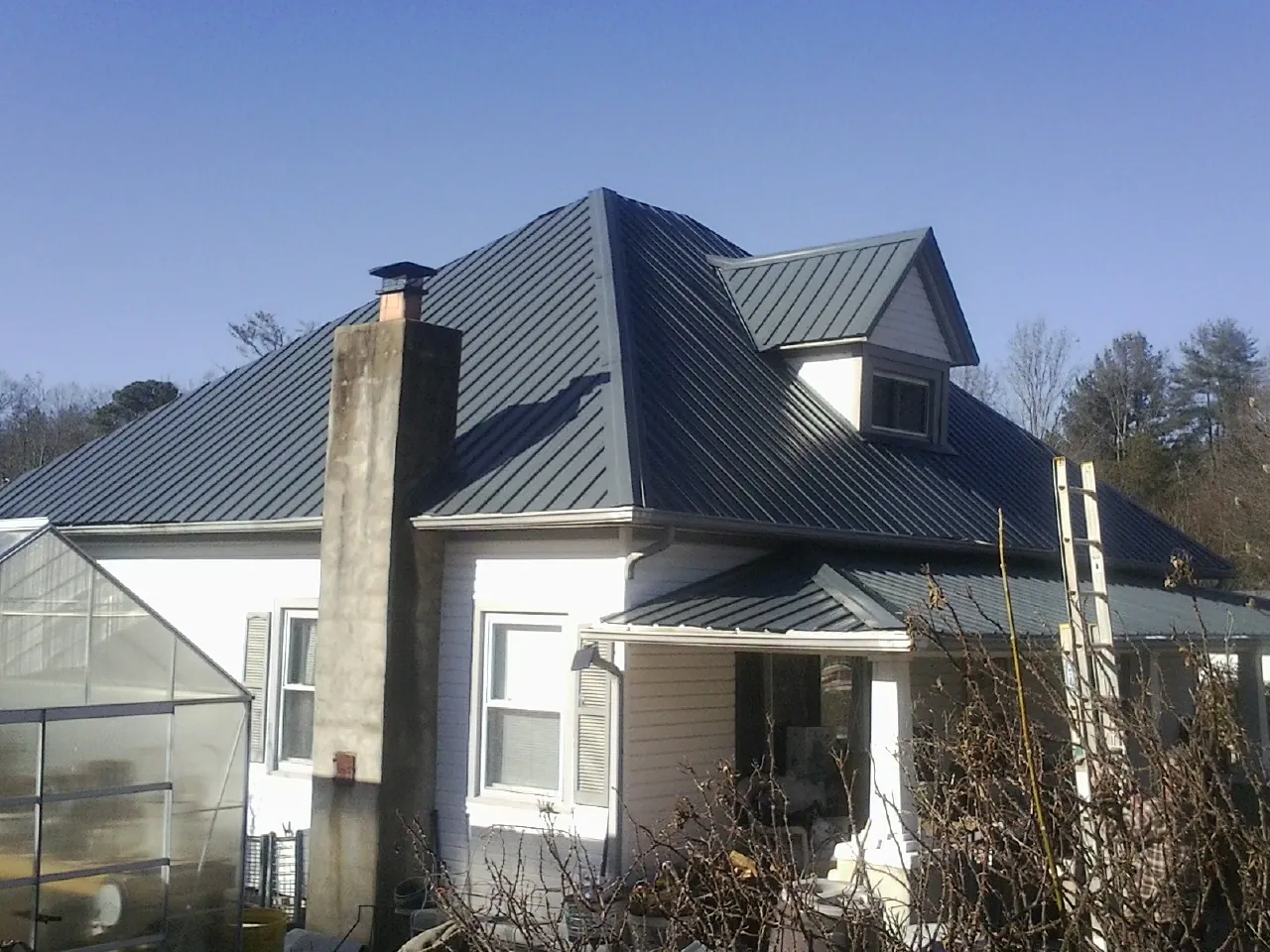 Dark blue standing seam metal roof on a white farmhouse with dormer — Slate & Tile Roof Repair by Roofing Brothers in Meherrin