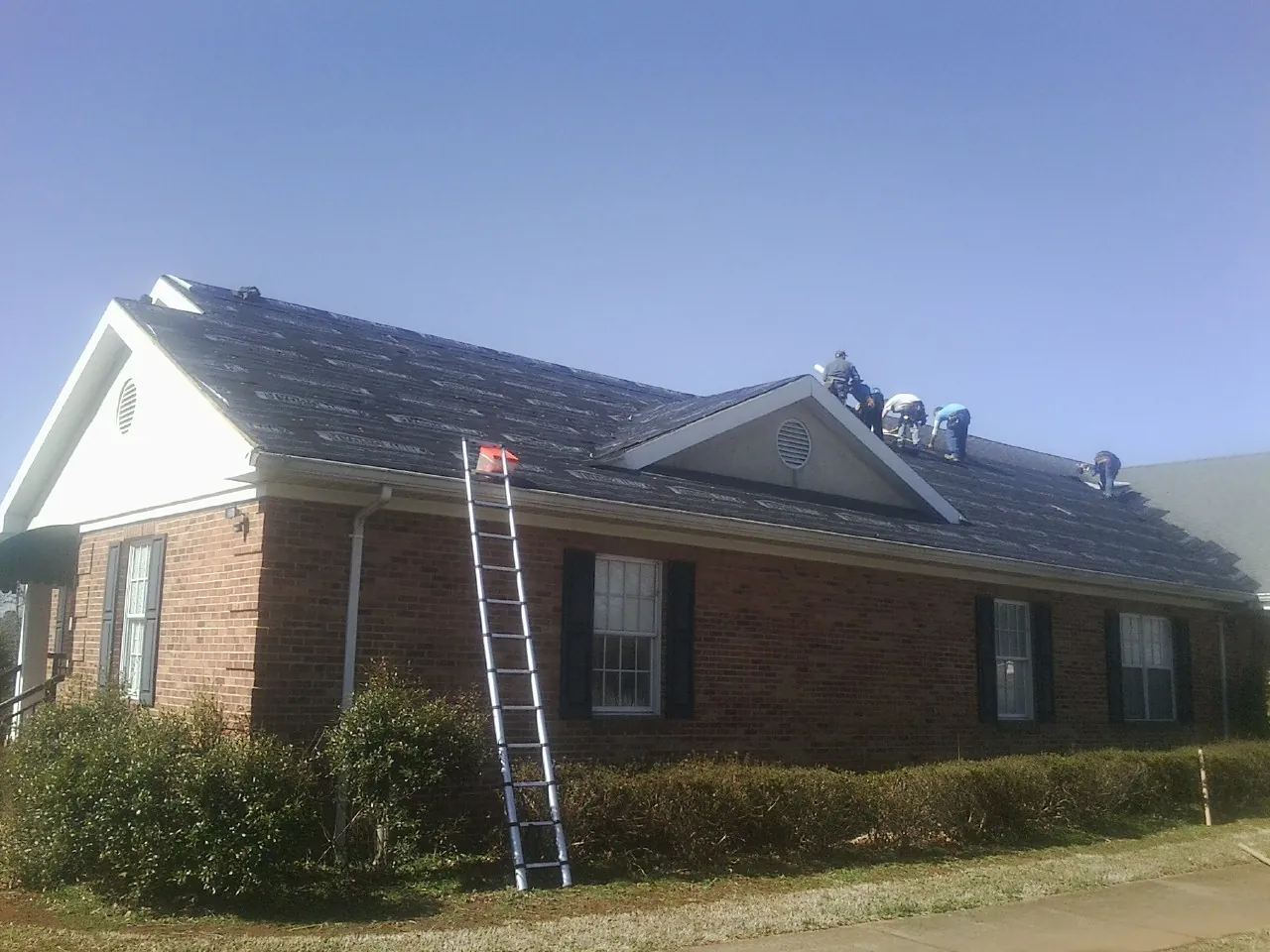 Crew tearing shingles off a brick ranch roof with a ladder set — Emergency Roof Repair work by our crew in Meherrin