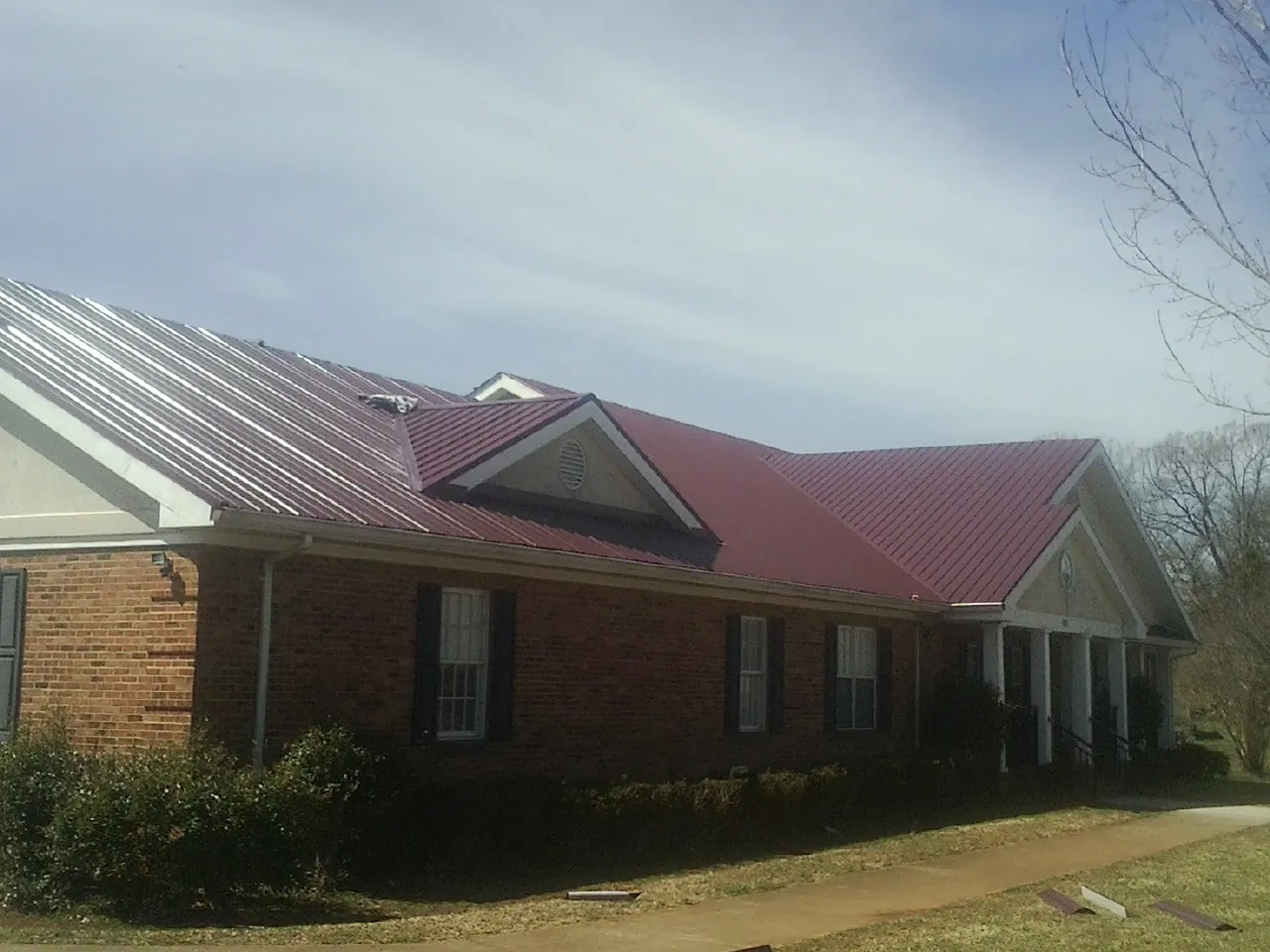 Red metal roof with gabled entries on a long brick building, from a Hail Damage Roof Repair job in Meherrin