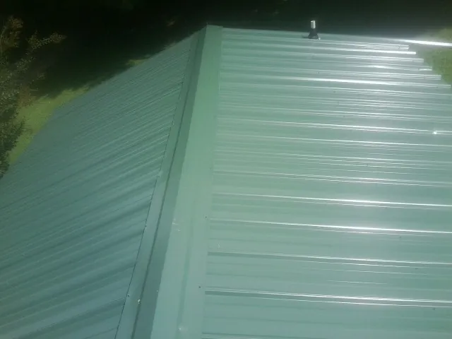 New green metal panels meeting at the ridge of a roof — Flat Roof Repair work by our crew in Meherrin