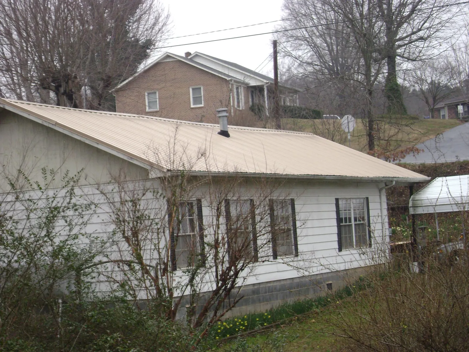Tan metal roof on a white sided house set into a hillside — Commercial Roofing by Roofing Brothers in Meherrin