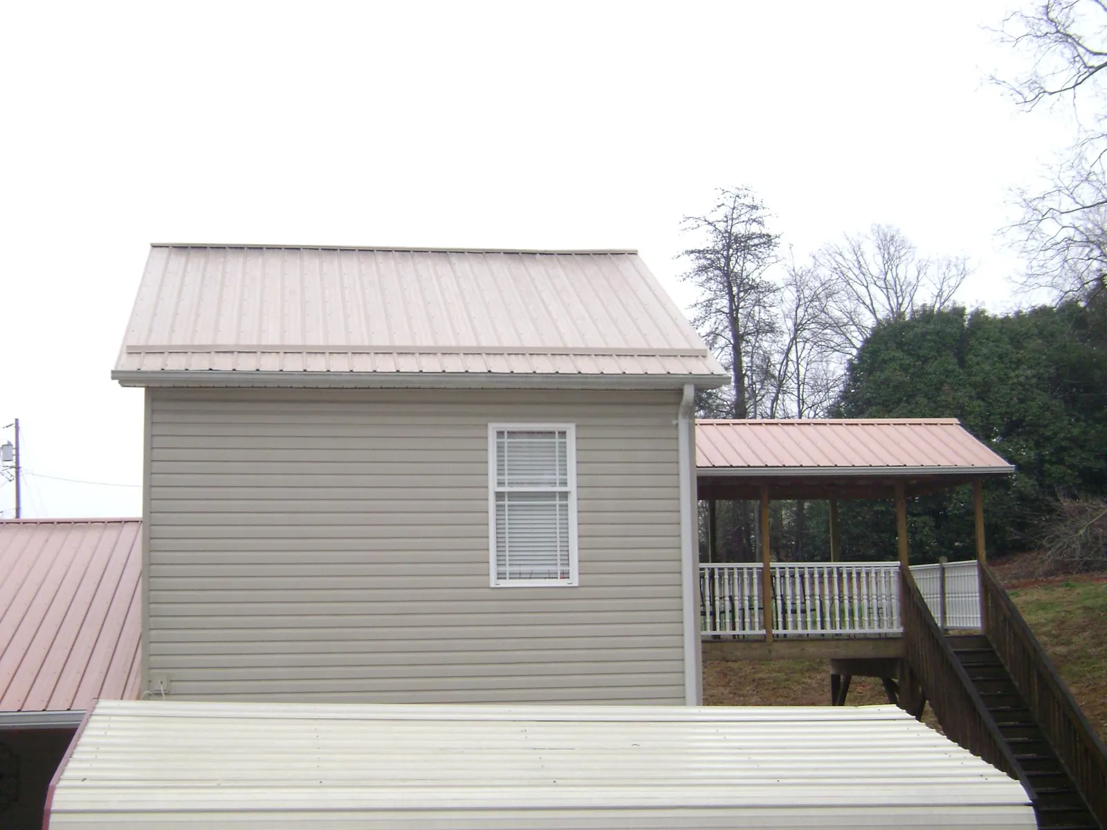 Tan metal roofs on a two story addition and attached porch, from a Roof Replacement job in Meherrin